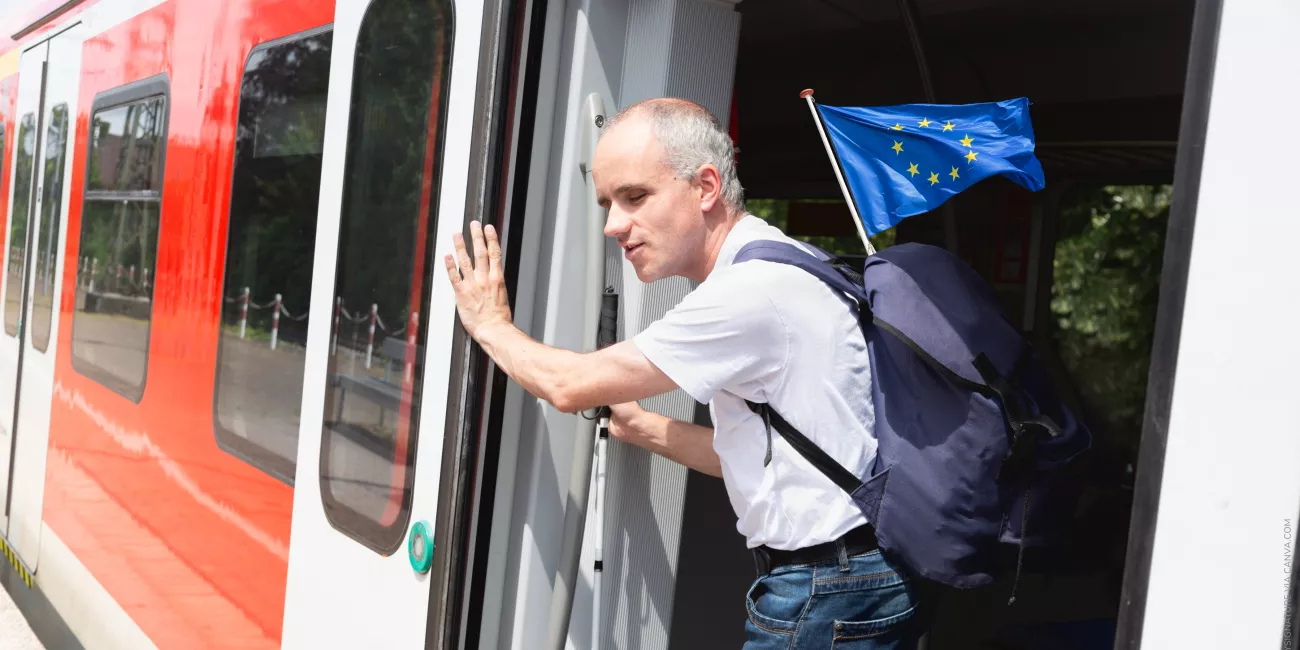Man with disability holding European Union flag stepping out from train
