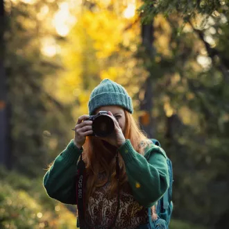 A young woman taking photos with a camera in an autumn forest