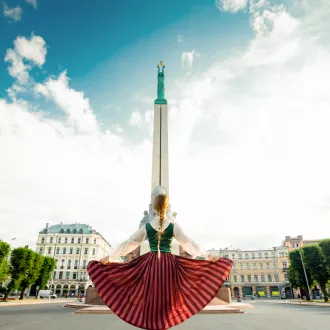 Girl in a Latvian clothes standing in front of monument of freedom