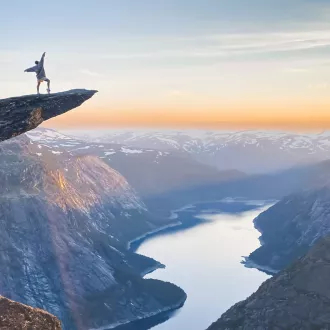 Person standing on the Trolltunga rock looking at the fjord and mountains